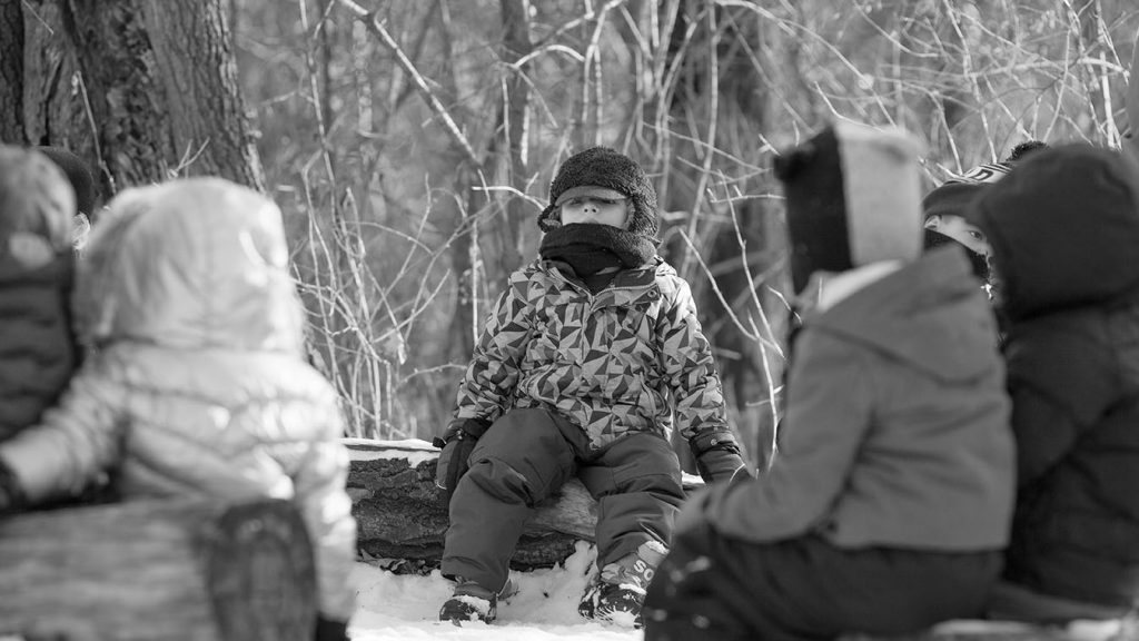 Child bundled up and sitting on a log outside in the snow
