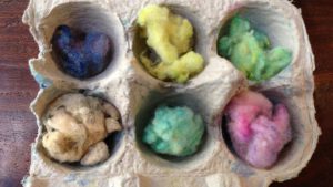 half of an egg carton with pieces of colorful dyed wool in each compartment