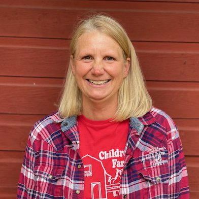 Children's Farm teacher Mickey Eckert standing in front of the red barn.