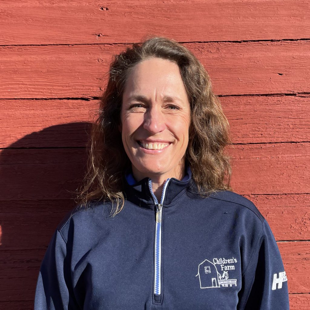 photo of teacher Jenny Jacobson standing in front of red barn wall